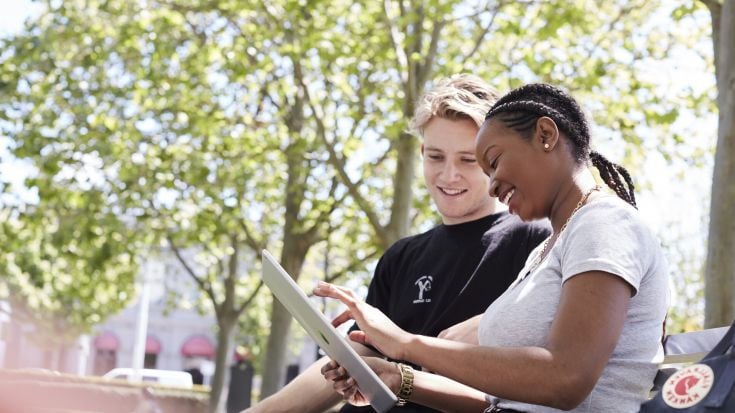 Two students sitting outside talking and laughing.