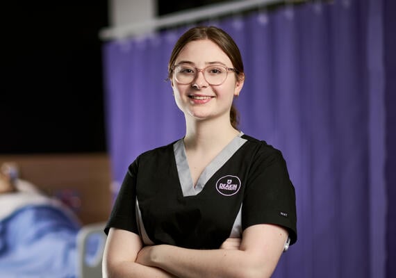 Nursing student Beth Lightbody looks at the camera with her arms crossed. She is wearing a nursing uniform.